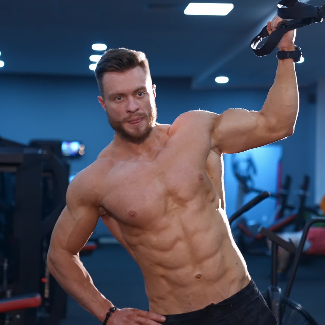 Strong handsome fitness trainer trains with a rope for side muscles. Naked torso with perfect muscles