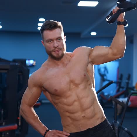 strong handsome fitness trainer trains with a rope for side muscles. naked torso with perfect muscles