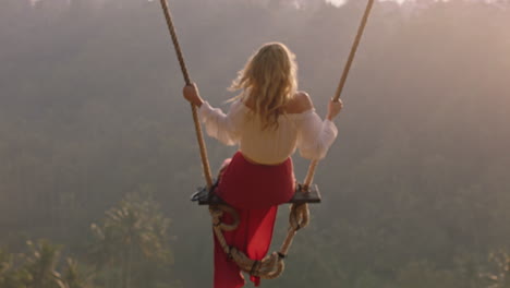 hermosa mujer balanceándose sobre el bosque al amanecer sentada en el columpio mirando a la cámara divirtiéndose disfrutando de la libertad en un estilo de vida de vacaciones exóticas en cámara lenta