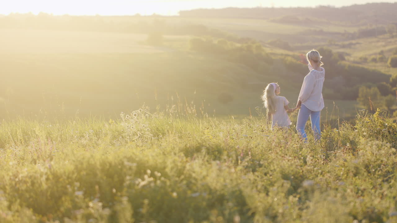 일몰 찾기에 녹색 초원을 보고 필드 위에 작은 딸과 함께 걷는 젊은 귀여운 여자