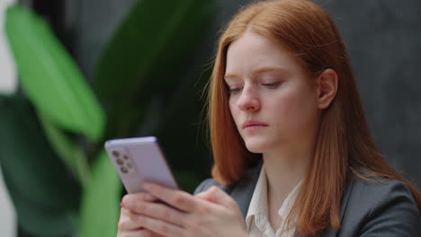 Beautiful young business woman using phone in office. Woman using a smartphone and leaning on a window texting sending emails planning meetings networking online browsing messages on mobile phone