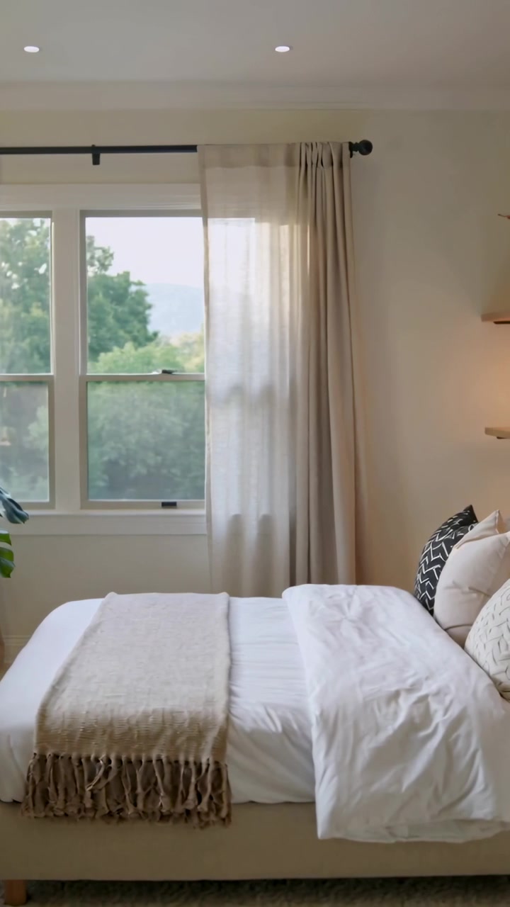 Video verticale: Telecamera che panoramica rivelando un letto in camera da letto per mostrare un piumone bianco e un plaid beige.