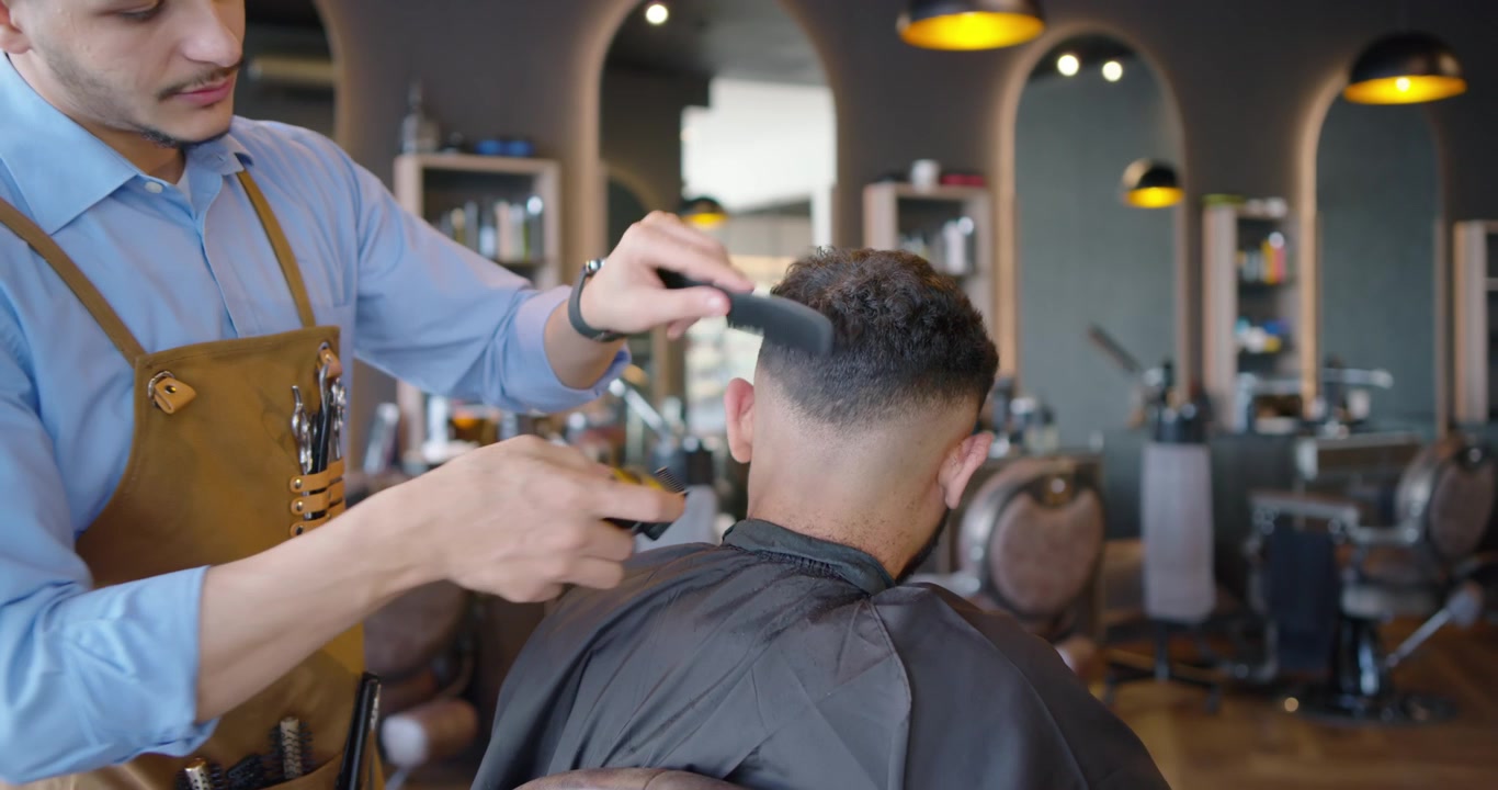 Afroamerikansk frisør klipper og udjævner kundens hår i salonen efter kundens ønske med en klippemaskine.