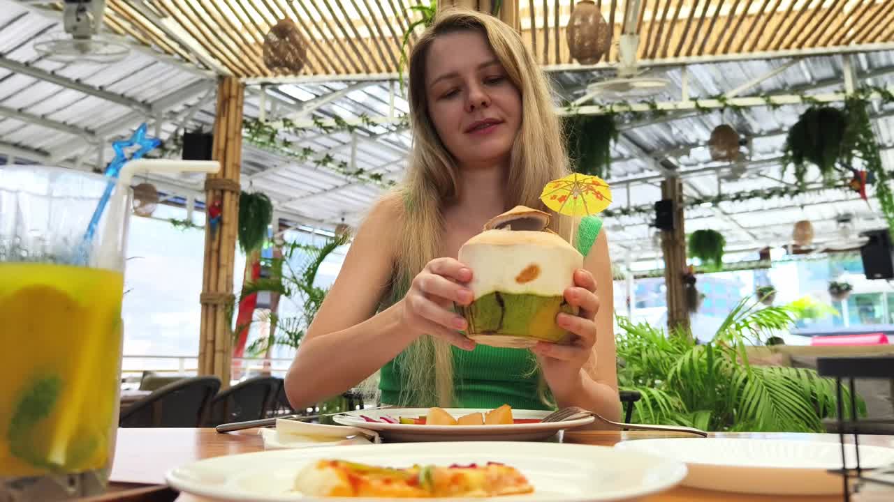 una mujer disfrutando de una bebida de coco y pizza en un café tropical.