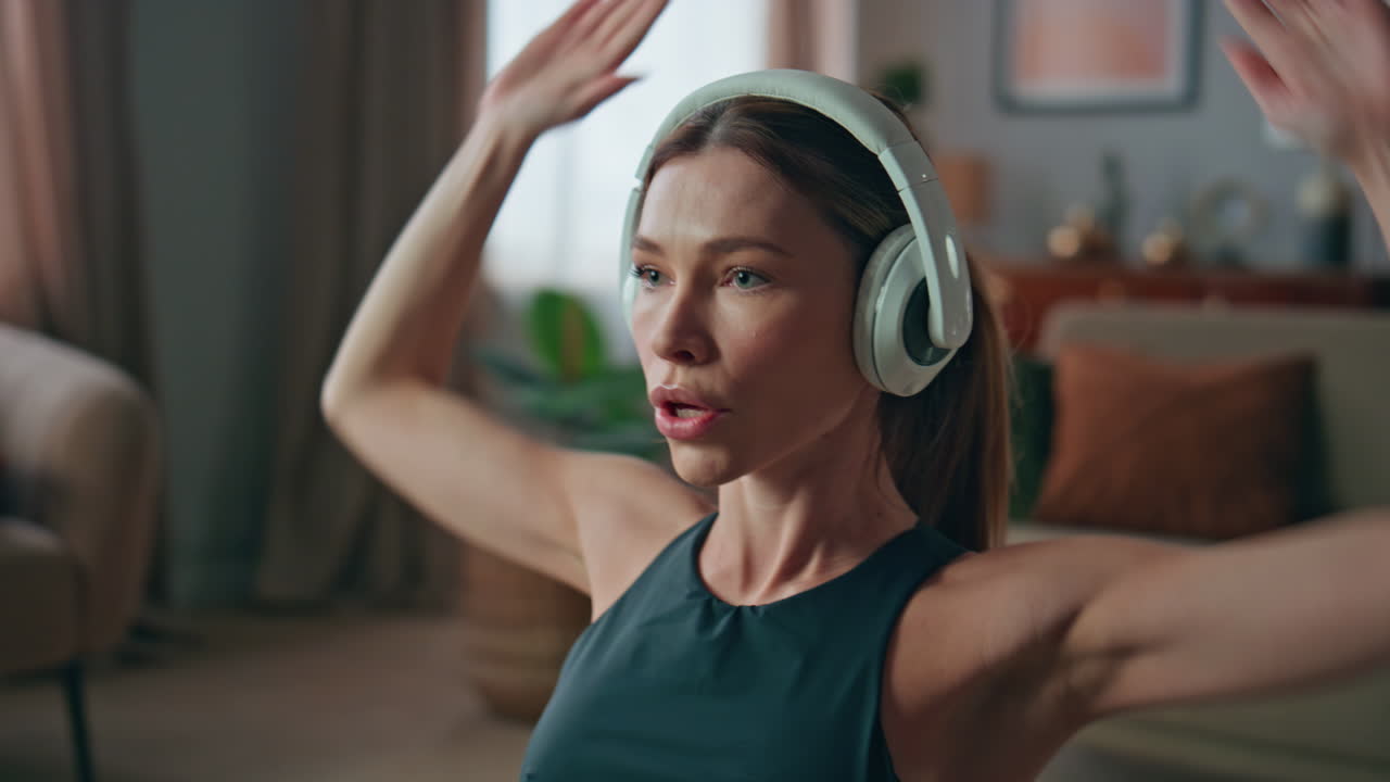 Closeup sportswoman bending body raising hands at home training. Girl headphones