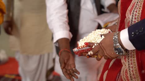cinematic shot of a hindu couple throwing puffed rice (khoi daan) in fire in presence of brahmin during a traditional hindu wedding in india