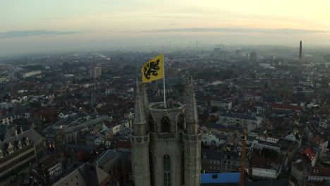 aerial parallax shot of old bell tower with flag of flanders, ghent, belgium