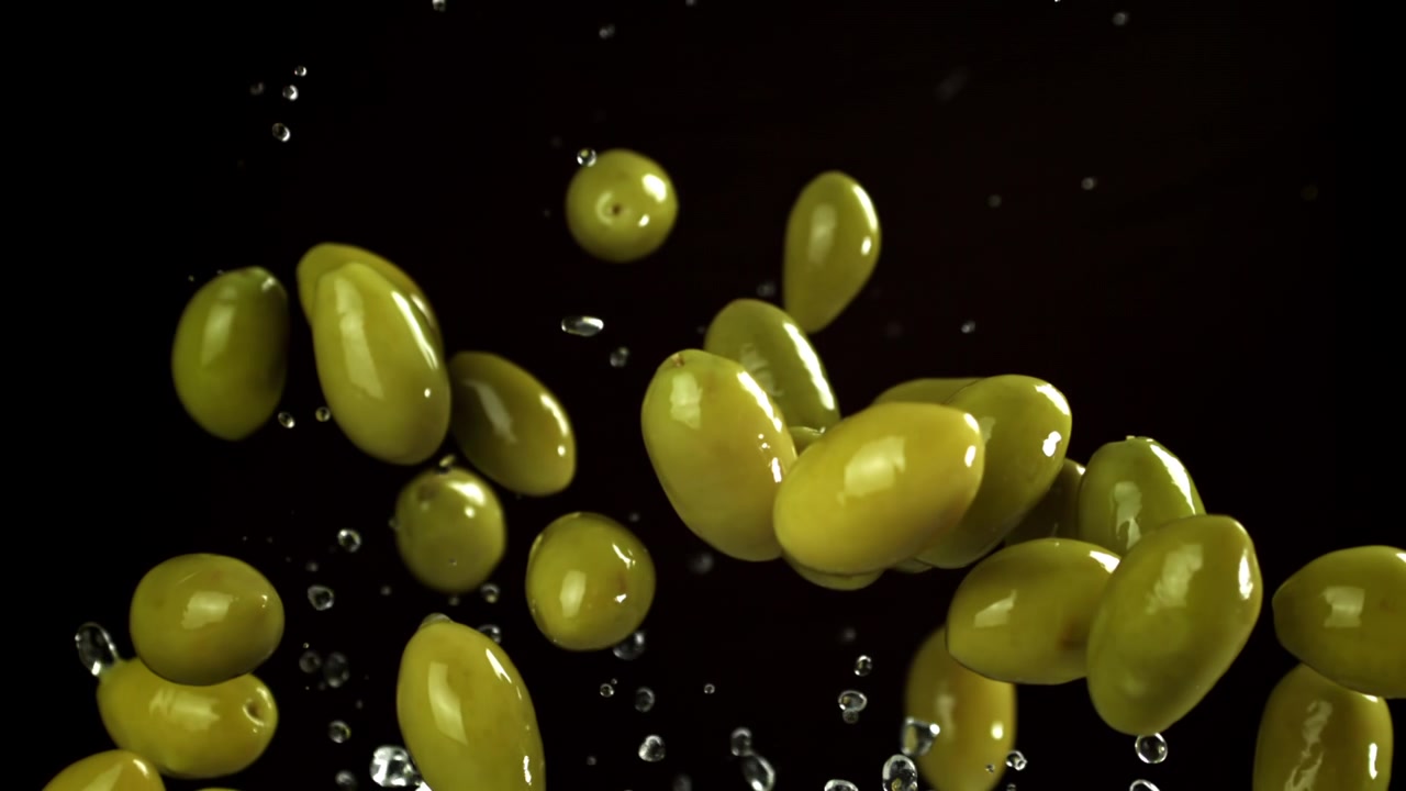 Olive verdi fresche e acqua che schizzano su sfondo nero