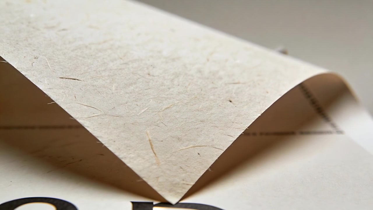 Fold løfter krøllet tekstureret beige papir, der danner en spids ved skrivebordet og afslører fed sort tekst nedenunder.