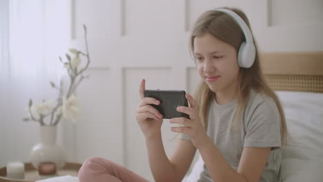 teen girl is listening music by headphones connected with smartphone by wifi sitting at her room at home