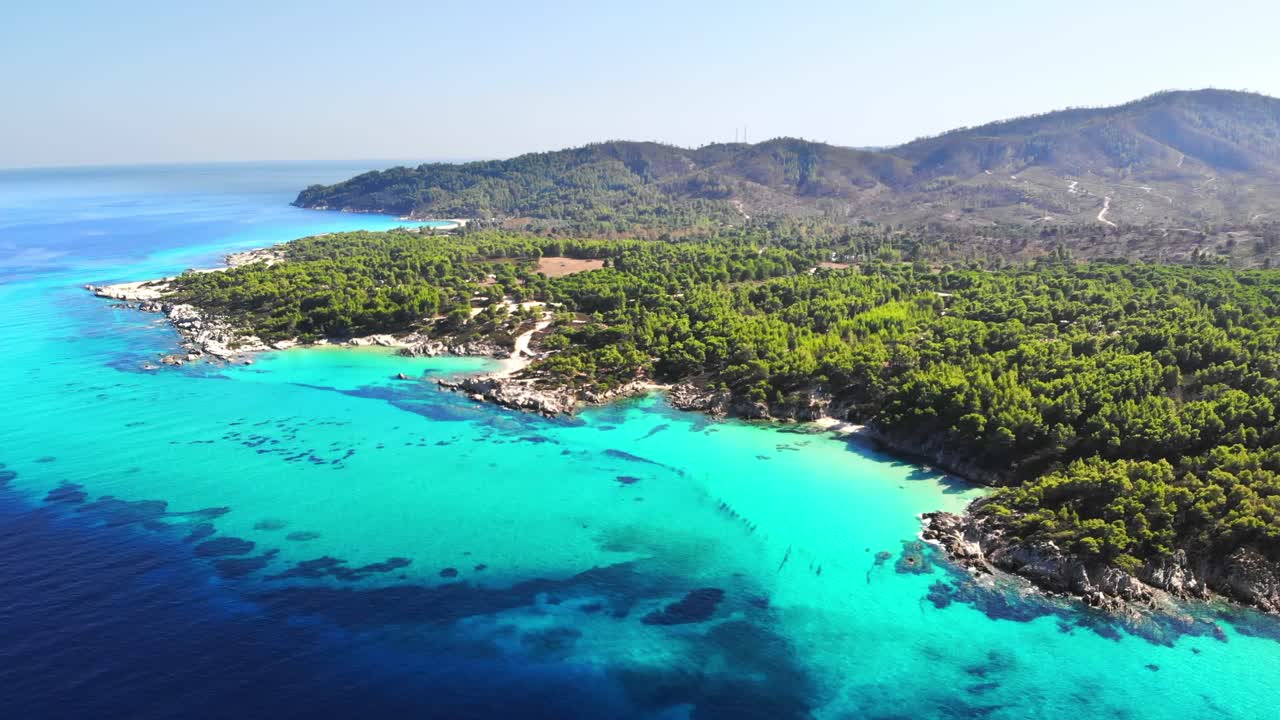 Aerial drone view of the Aegean sea rocky coast with blue transparent water, multiple greenery, hills. Greece