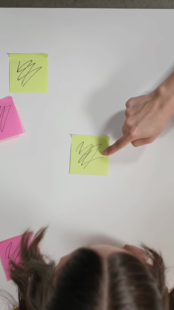 Vertical video: Reaching for post-it, kid placing and folding notes on white table in yellow top