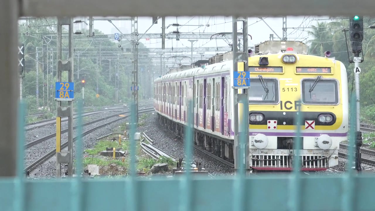 Un treno locale sta arrivando alla stazione di Malad sotto la pioggia a Mumbai, India