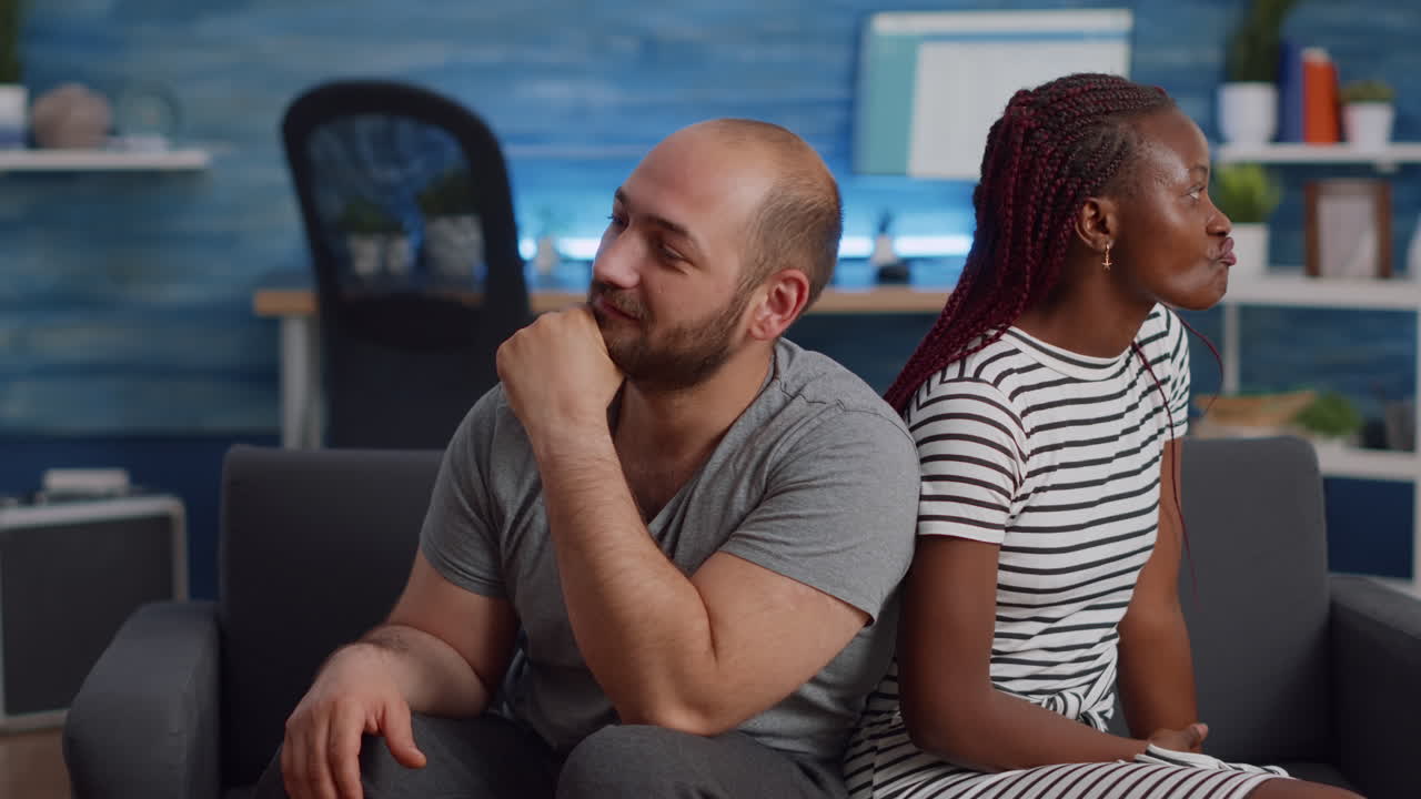 Irritated interracial couple fighting and sitting on couch