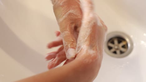young woman in a red robe washes her hands under running water in a modern bathroom with a round illuminated mirror. high quality 4k footage