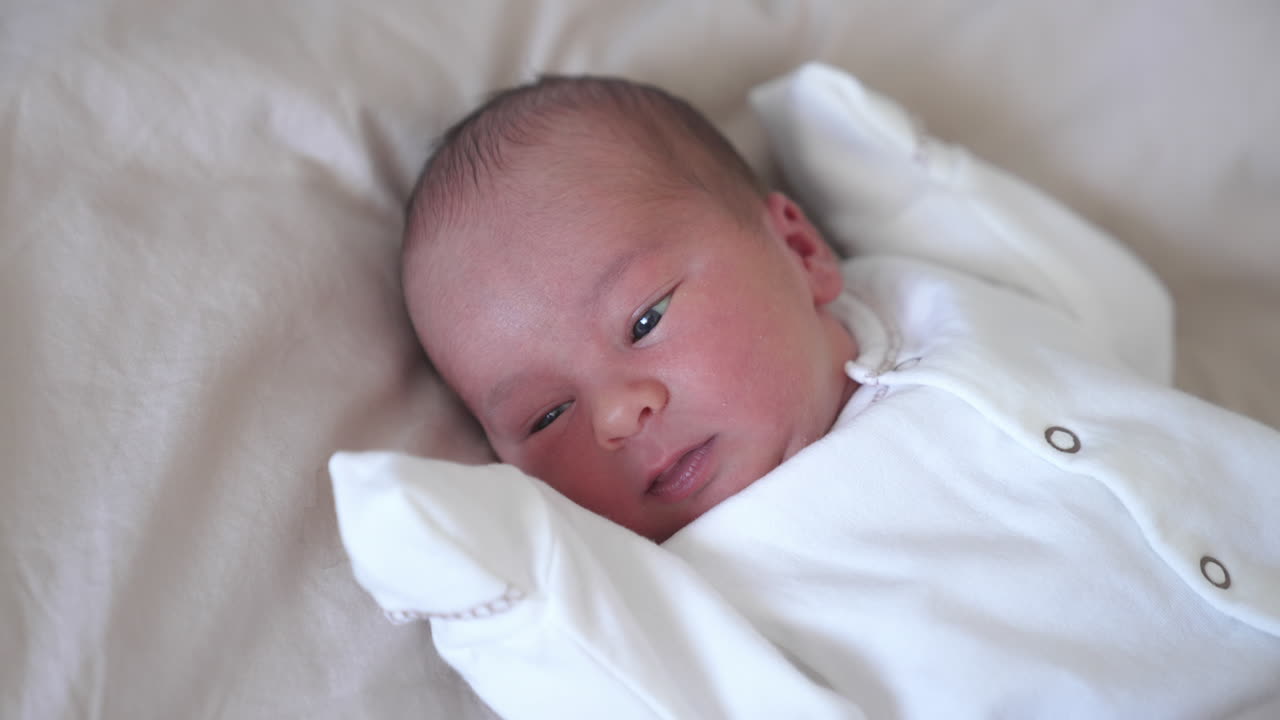 Little baby looks intensely at his hand then sneezes and stars to cry. Quickly changing mood of a child. Close-up.