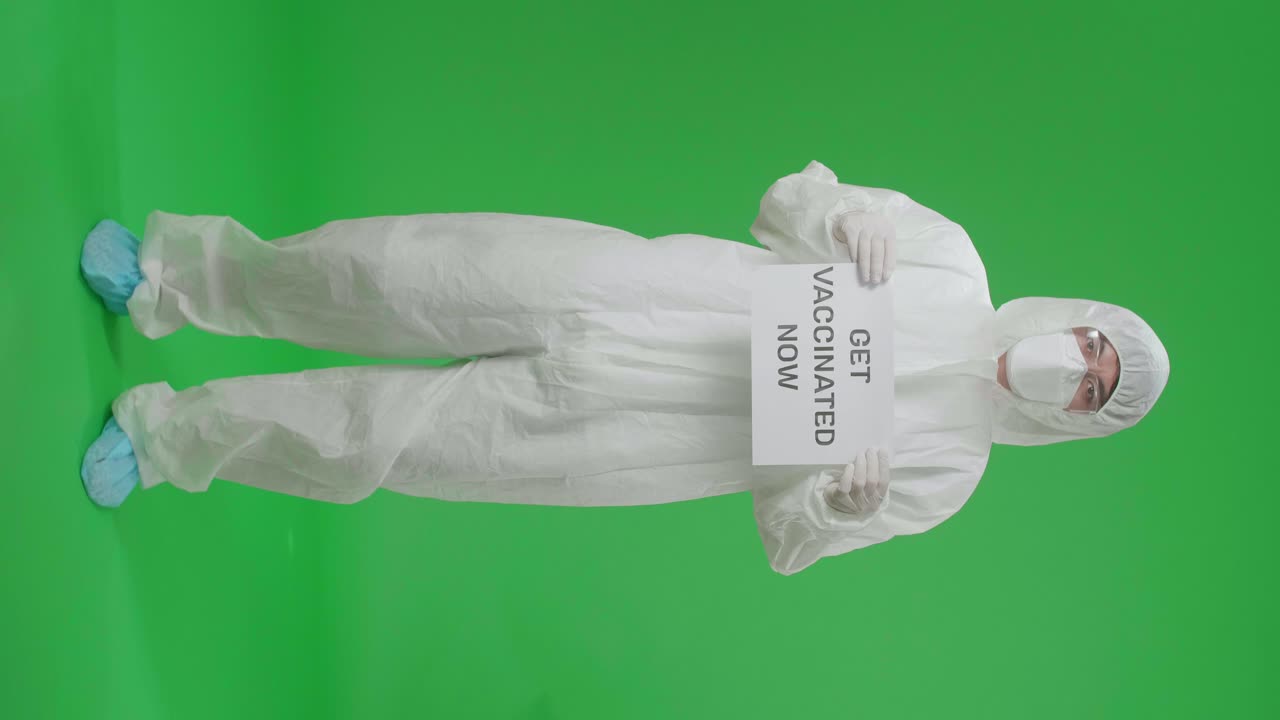 Person in Protective Gear Holding a Sign Saying 'Get Vaccinated Now'