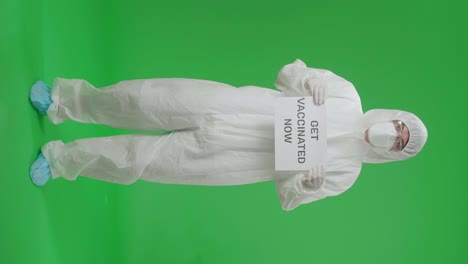 person in protective gear holding a sign saying 'get vaccinated now'