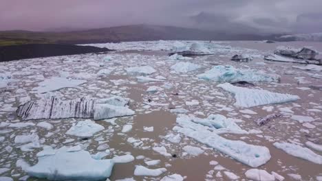 Toma-Aérea-Inclinada-Hacia-Abajo-De-Una-Enorme-Laguna-Glaciar-Llena-De-Icebergs-Flotantes