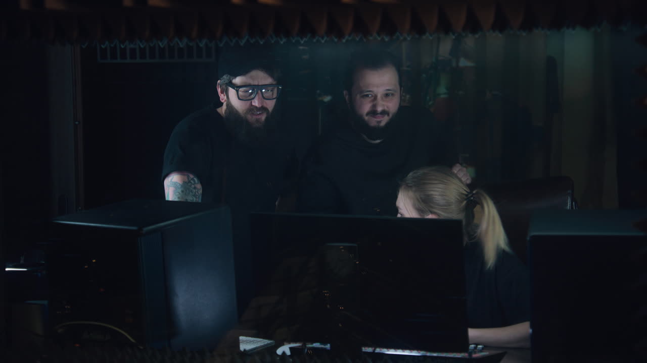 Professional female audio engineer or producer edits new album at soundproof room. Band of musicians work in sound recording studio. Computer with musical equipment on table. Music production concept.