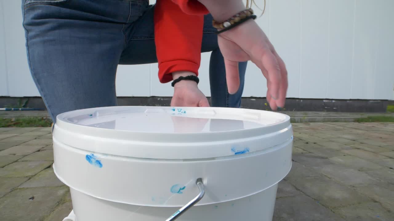 한 소녀 의 손 이 파란색 페인트 를 넣은 페인트 버 을 열고 있는 것