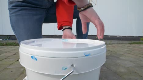 close up slow motion of a girls hand is opening a paint bucket wih blue paint