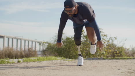 deportista enfocado con una pierna artificial corriendo desde el comienzo de crouch en el parque por la mañana