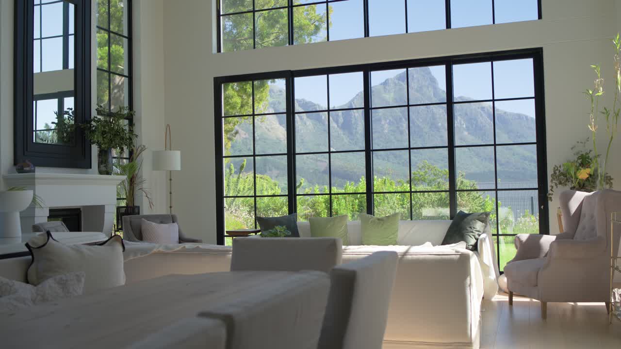 La cámara se desplaza lentamente hacia la izquierda y hacia adelante, revelando una vista de la ventana, una chimenea y un sofá iluminado por el sol