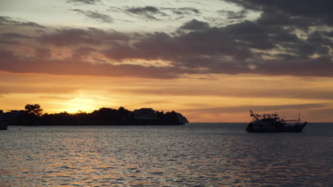 Silhouetted-Moored-Fisher's-Boat-with-Beautiful-Golden-Sunset-Background,-Round-Solar-Disc-Facing-Tropical-Island-at-Kota-Kinabalu-Waterfront