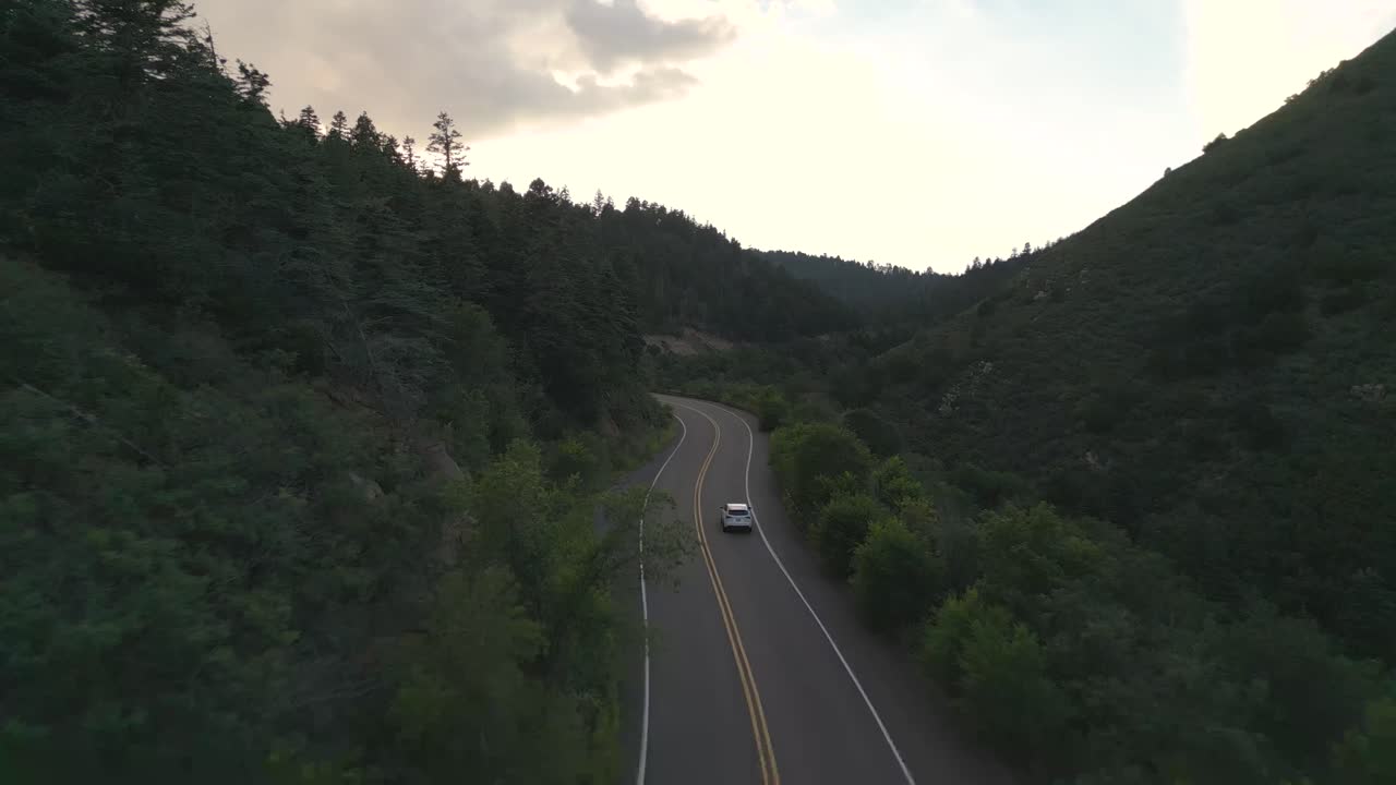 Ripresa aerea con drone di un'auto bianca che si muove su una strada deserta nella campagna americana al crepuscolo.