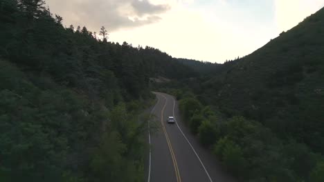 tracking aerial view of white car moving on empty road in american countryside at twilight, drone shot