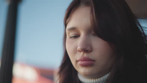 close-up of young girl with pink lips, slightly downcast eyes, and nose ring, focusing with thoughtful expression, hair fluttering in the wind, soft natural light, blurred background