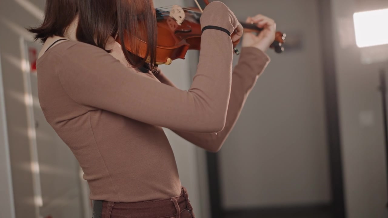 Female artist finetuning her violin. She adjusts her violin with precision during warmup session. Female musician finetunes her violin and bow storing concentration before rehearsal