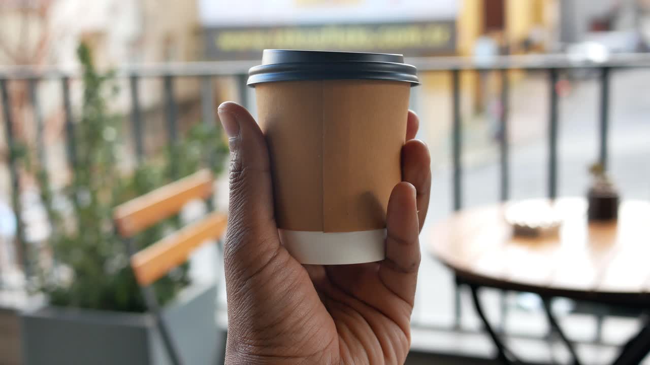 persona sosteniendo una taza de café desechable en una cafetería al aire libre