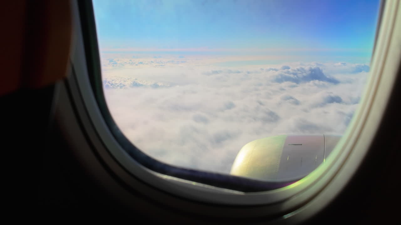 View from an airplane window of the wing gliding above a vast sea of clouds, with the horizon and a blue sky above