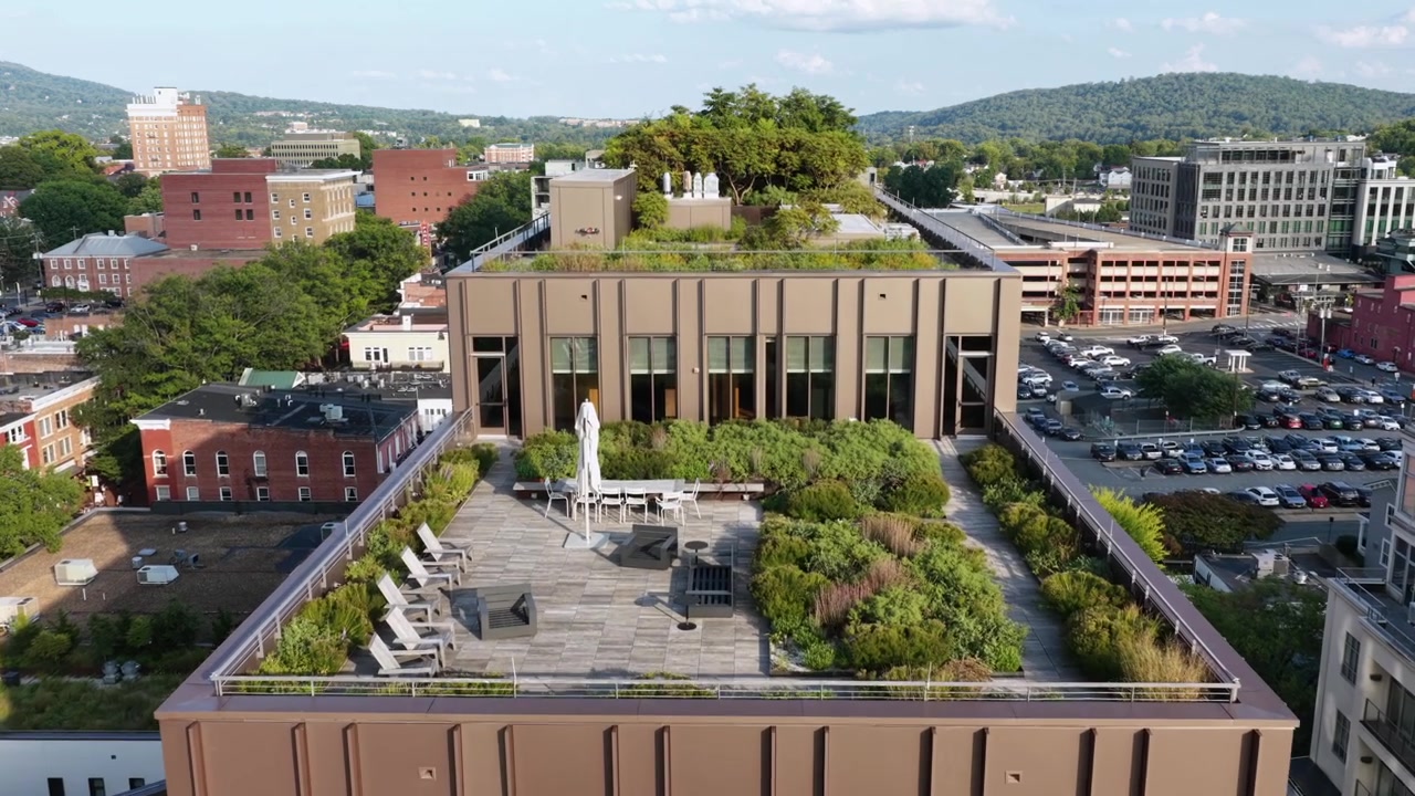 Moderno edificio in mattoni marroni con terrazze giardino nel centro di Charlottesville, in Virginia, circondato da blocchi di mattoni più antichi, parcheggi e lo skyline delle Blue Ridge. Ripresa aerea in avvicinamento