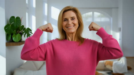 smiling senior woman flexing muscles in pink sweater