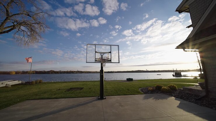 canestro da basket su un campo accanto a una casa di lusso sul lago con la bandiera americana che sventola sullo sfondo, perdite di luce solare
