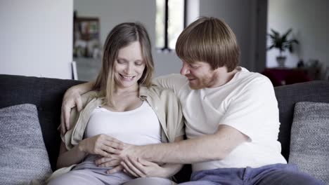 happy couple sitting on sofa and touching belly