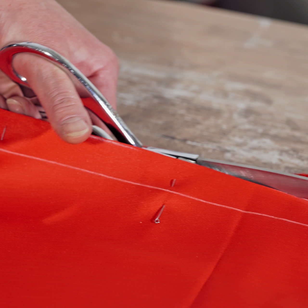 Tailor is cutting red fabric with sharp scissors at table in atelier. Woman's hands cutting bright red fabric on sketch lines by metal scissors. Feminine hobby. Close-up.