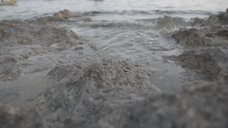 Nahaufnahme-Von-Wasser,-Das-In-Küstennähe-Auf-Einige-Felsen-Trifft-Und-Baumstämme-In-Zeitlupe-Spritzt