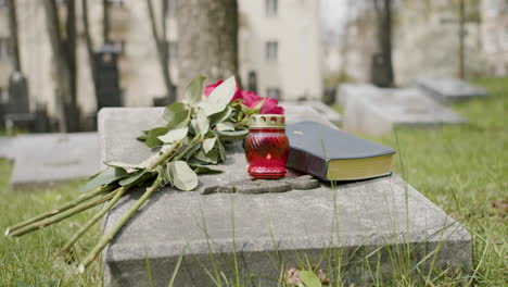 vista frontal de rosas rojas, biblia y velas en una lápida en un cementerio