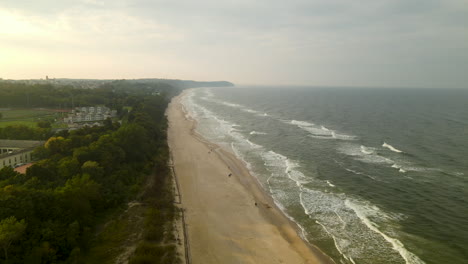 Drohne-Fliegt-über-Leeren-Strand-Zurück,-Wellen-Schlagen-Bei-Sonnenuntergang-An-Einem-Bewölkten-Abend-Gegen-Das-Ufer