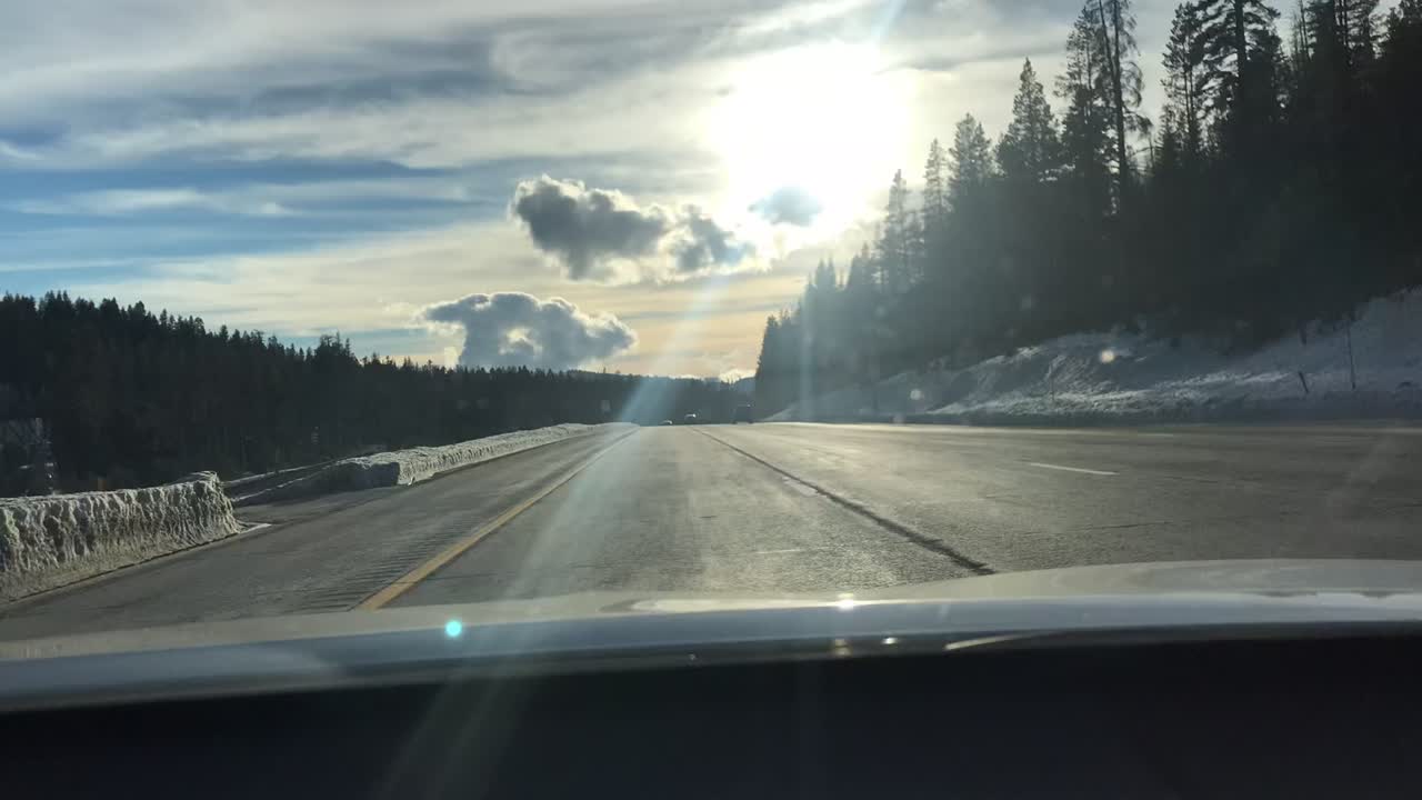 Time lapse shot of a car as it travels down a country highway through snowy mountains, sun and clouds, other vehicles can been seen in the adjoining lanes