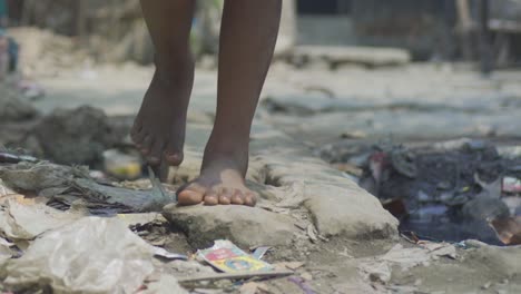 young indian poor orphan girl, walking on road with naked dirty feet near garbage, rural village