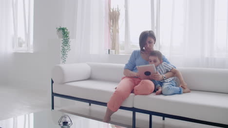 madre e hijo sentados en el sofá usando tableta digital. madre feliz y niño pequeño usando tableta con pantalla táctil juntos viendo un video. madre sonriente y niño lindo jugando en tablet digital.