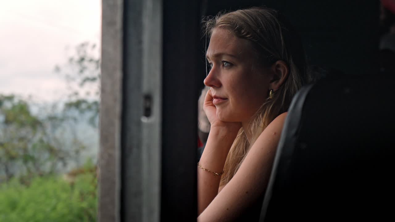 A woman gazes thoughtfully through the window of a moving train traveling the scenic Ella to Kandy route in Sri Lanka.