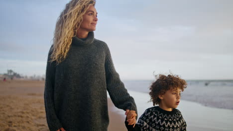 relaxed mother walking son along ocean shore. happy family spending weekend