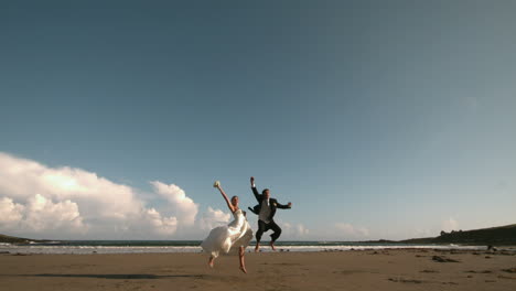 Glückliches-Frisch-Vermähltes-Paar-Springt-In-Die-Luft-Am-Strand