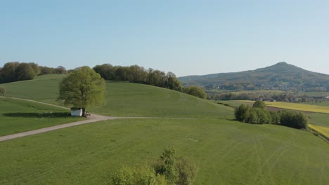 drone - toma panorámica aérea de la capilla solitaria en un campo con césped y una carretera con un tractor y un panorama de las siete montañas - siebengebirge 30p
